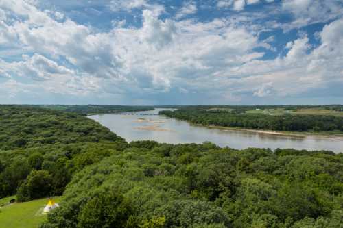 A scenic view of a river winding through lush green forests under a partly cloudy sky.