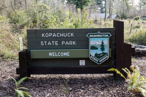 Welcome sign for Kopachuck State Park in Washington, surrounded by trees and natural scenery.