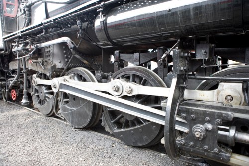 Close-up of a vintage steam locomotive's wheels and drive mechanism, showcasing intricate metalwork and engineering.