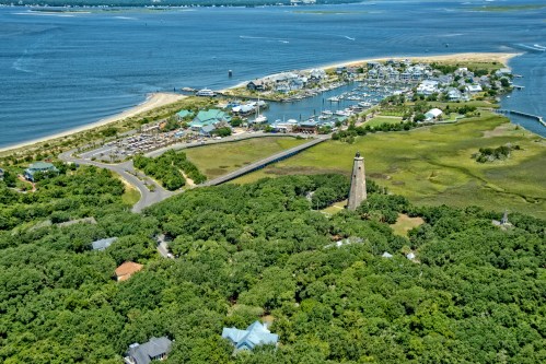Aerial view of a coastal area with a lighthouse, marina, and lush greenery along the shoreline.
