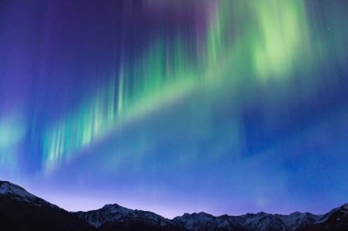 A stunning display of the northern lights illuminates the night sky above snow-capped mountains.