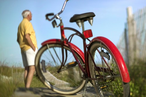 A red bicycle in focus with a man in a yellow shirt standing in the background, overlooking a scenic path.