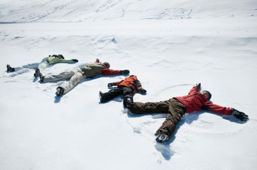 Four people lying in the snow, making snow angels in a winter landscape.