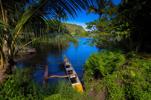 A serene river scene with lush greenery and a colorful canoe resting on the bank under a clear blue sky.