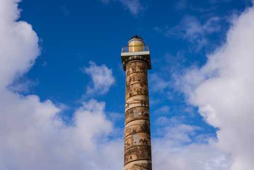 A tall lighthouse with decorative murals stands against a blue sky with fluffy clouds.