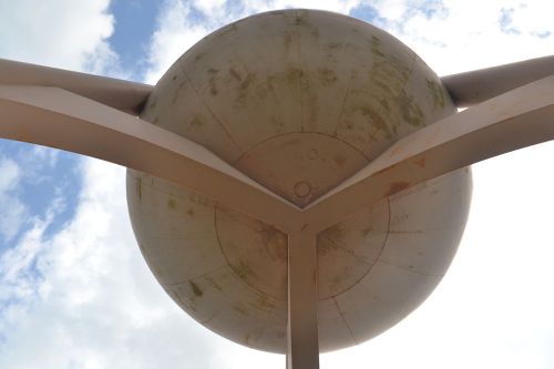 A large, spherical sculpture mounted on a metal structure against a cloudy sky.