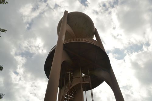 A tall water tower with a spherical top, surrounded by cloudy skies.