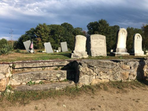 A cemetery with several gravestones, some leaning, and a stone wall with steps leading into the area.