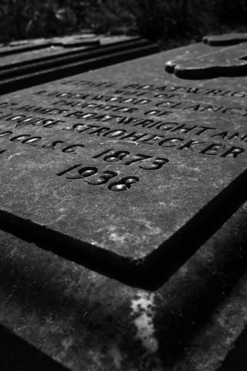 Close-up of a weathered gravestone with engraved text, partially obscured by dirt and shadows.