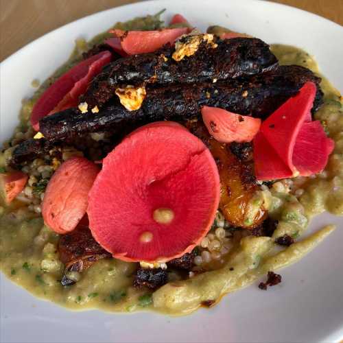 A colorful dish featuring roasted vegetables, pink radish slices, and a creamy base, garnished with herbs.