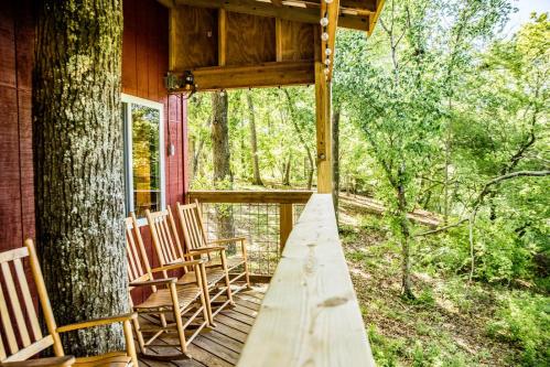 A wooden porch with rocking chairs overlooks a lush, green forest. Sunlight filters through the trees.