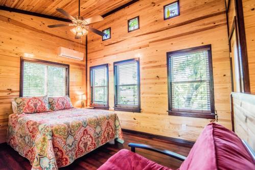 Cozy wooden bedroom with a colorful bedspread, ceiling fan, and large windows letting in natural light.