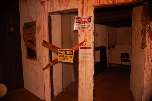 Two doorways with caution signs, one marked "Quarantine Area," and blood splatters on the walls, creating a creepy atmosphere.