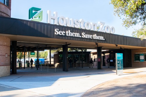 Entrance to Houston Zoo with a sign that reads "See them. Save them." and visitors entering the facility.