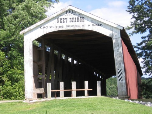 A historic covered bridge with a wooden structure, marked "Neet Bridge" and built in 1904, surrounded by greenery.