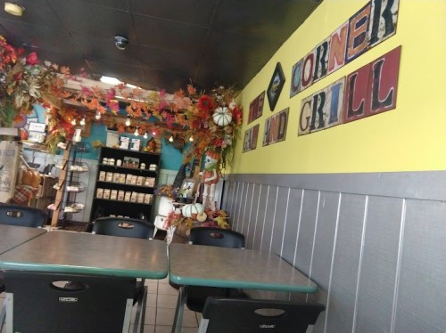 Cozy diner interior with colorful decor, tables, and a wall sign reading "The Corner Grill." Autumn-themed decorations visible.