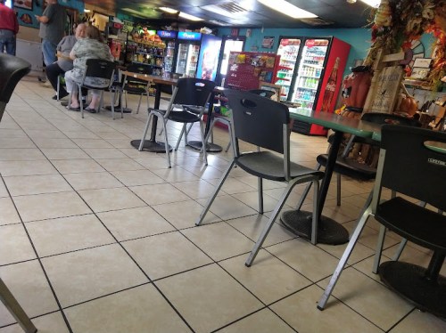 A casual dining area with empty chairs, tables, and vending machines in the background.