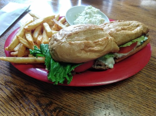 A plate with two sandwiches, lettuce, tomato, and fries, accompanied by a small bowl of coleslaw.