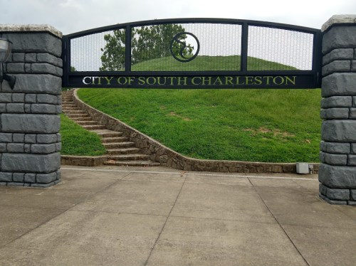 Archway sign reading "City of South Charleston" with grassy hill and stone steps in the background.
