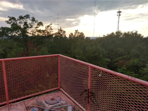 View from a pink metal observation deck overlooking a forested area with communication towers in the distance.