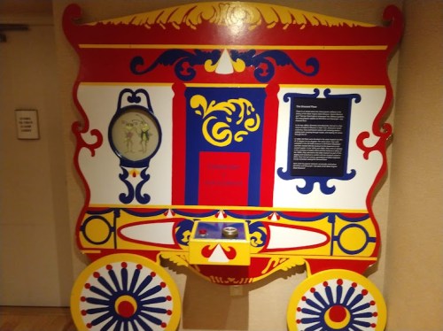 Colorful decorative display resembling a traditional cart, featuring intricate designs and a central circular mirror.