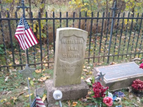 Gravestone of Curtis King, 1844-1863, surrounded by flowers and small American flags in a cemetery.