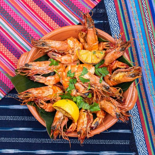 A vibrant dish of shrimp garnished with lime and herbs, served in a clay bowl on colorful woven textiles.