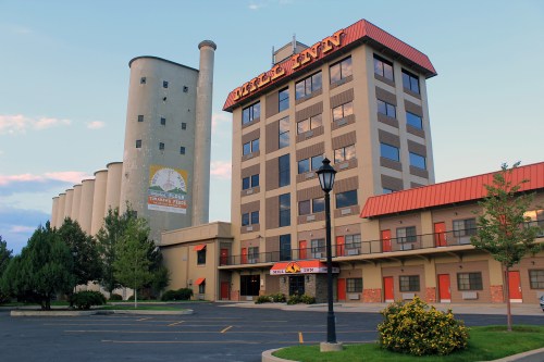 A hotel building with a modern design, featuring a red roof and adjacent silos, surrounded by trees and a parking lot.