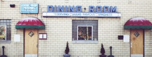 A restaurant exterior featuring a sign that reads "Dining Room" and "Serving Maria's Famous Spaghetti" with awnings.