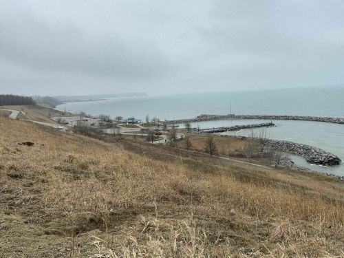 A cloudy day over a lake, with a grassy hill in the foreground and a rocky pier in the distance.