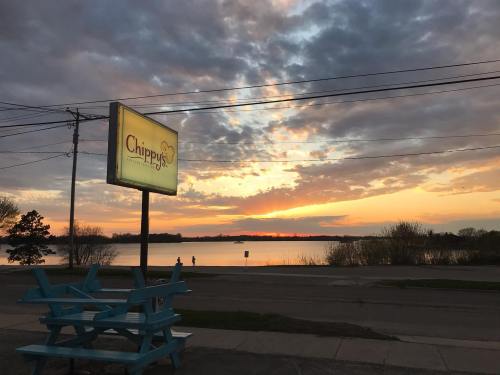 A serene lakeside view at sunset, with a sign for "Chippy's" and a blue bench in the foreground.