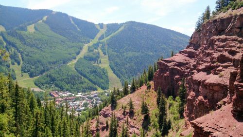 A scenic view of mountains with ski slopes, overlooking a small town nestled in a valley surrounded by trees.