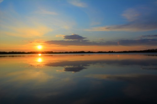 A serene sunset over a calm lake, with vibrant colors reflecting on the water's surface.