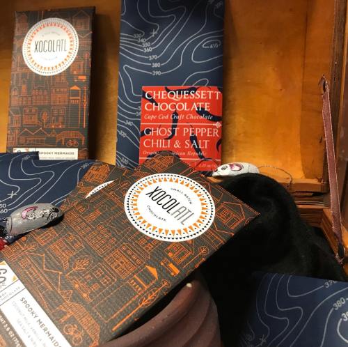 Assorted chocolate bars displayed in a wooden box, featuring flavors like ghost pepper chili and salt.