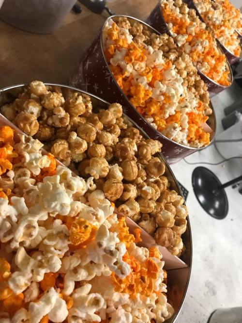 Three festive tins filled with a mix of caramel and cheese popcorn, arranged on a countertop.