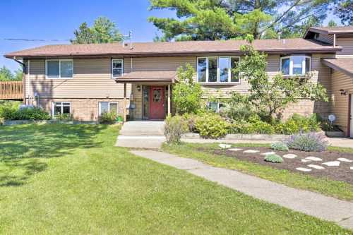 A two-story house with a red door, surrounded by greenery and a well-maintained lawn.