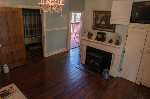 Cozy interior with wooden floors, a fireplace, chandelier, and a doorway leading to a deck.