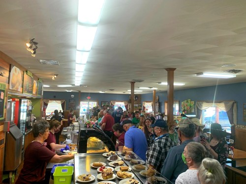 A busy cafeteria with a long line of people serving and enjoying various dishes and desserts.