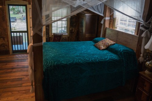 Cozy bedroom featuring a teal bedspread, wooden furniture, and natural light from windows.