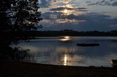 A serene lake at sunset, with clouds reflecting on the water and a small dock in the foreground.