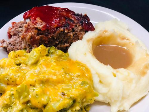 A plate with meatloaf topped with ketchup, cheesy broccoli, and creamy mashed potatoes with gravy.