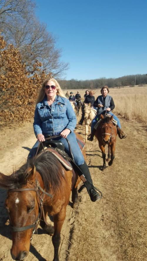 A group of people riding horses along a dirt path in a sunny, open field.