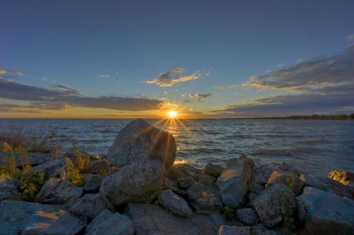 A serene sunset over a calm lake, with rocks in the foreground and colorful clouds in the sky.