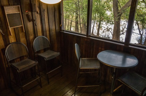A cozy wooden room with two metal chairs and a small round table, overlooking a view of trees outside.