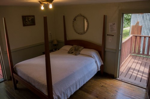 Cozy bedroom with a four-poster bed, wooden floors, and a door leading to a small deck outside.