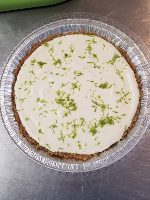 A round key lime pie with a graham cracker crust, topped with a smooth white filling and sprinkled with lime zest.