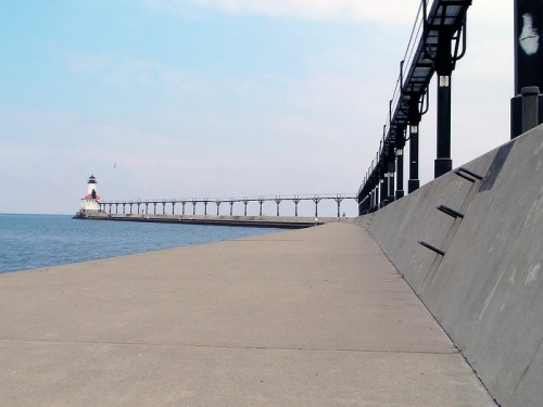 A long pier extends into calm waters, leading to a lighthouse under a clear sky.