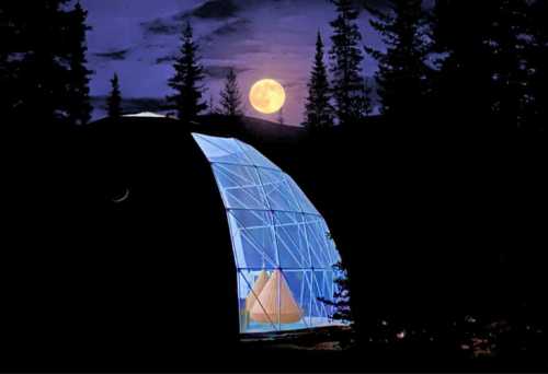 A glowing geodesic dome in a forest at night, illuminated by a full moon and surrounded by tall trees.