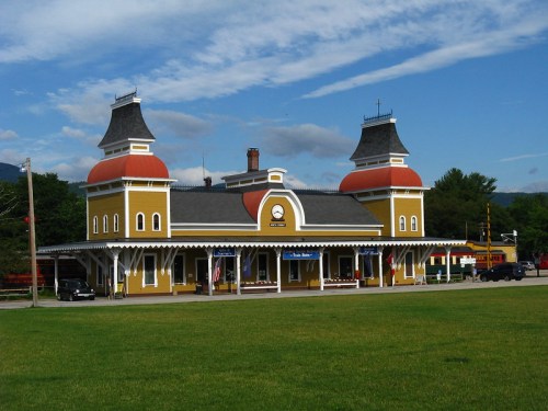 A colorful train station with yellow walls and red domes, set against a blue sky and green grass.