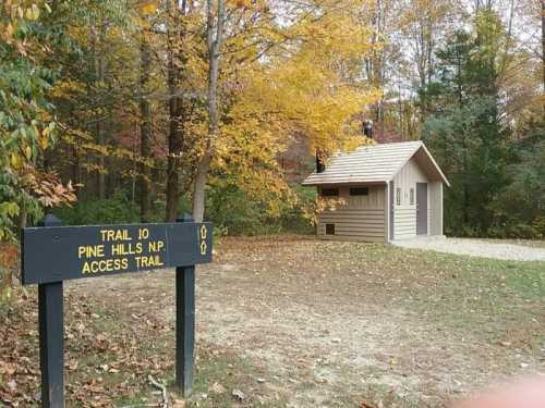 A sign for Trail 10 at Pine Hills National Park next to a small, rustic building surrounded by autumn foliage.